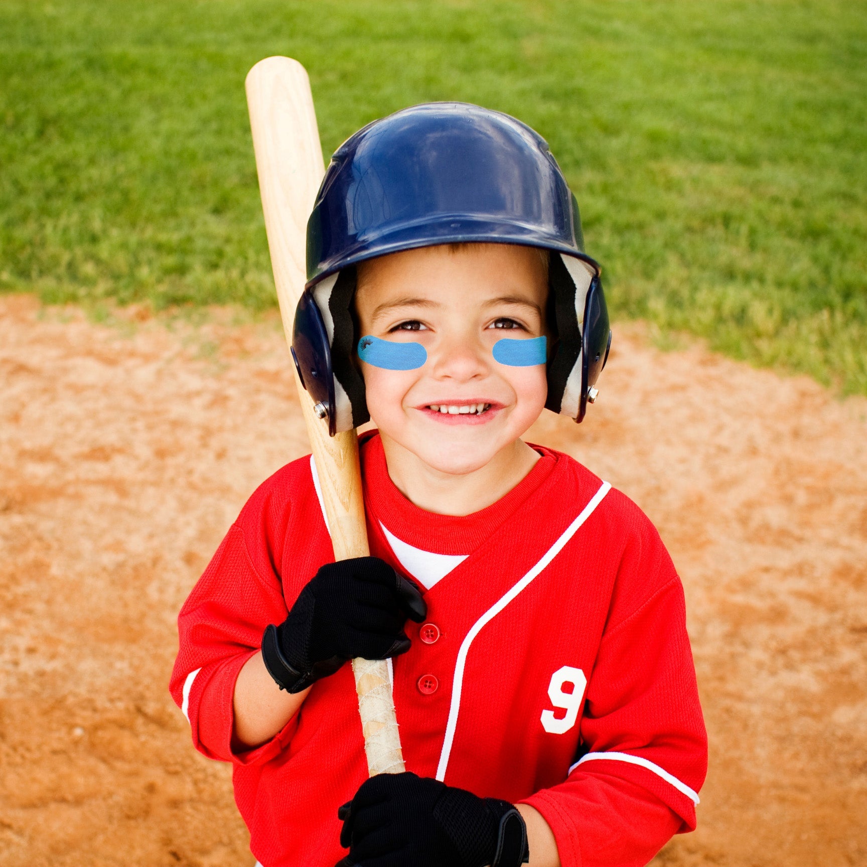 Child in a red baseball uniform with a bat and helmet on a baseball field