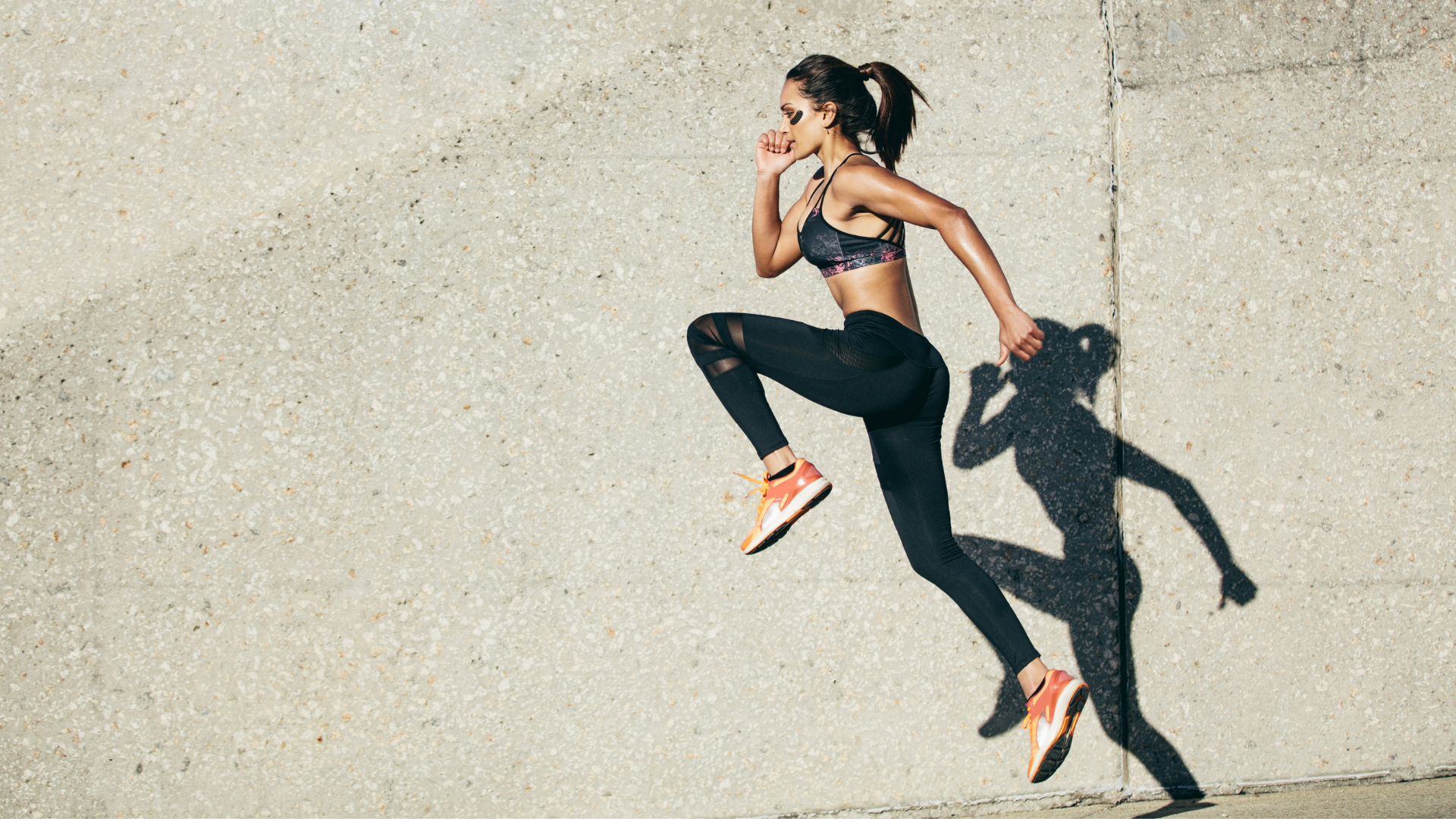 Woman running on a concrete surface with a wall in the background